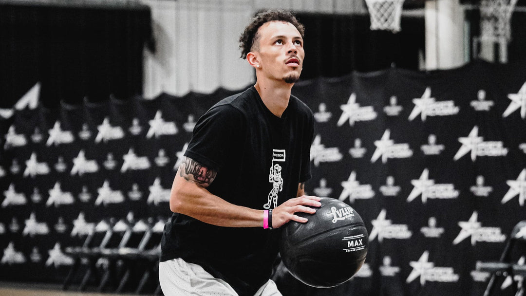 Person holding a basketball on a basketball court with a branded backdrop