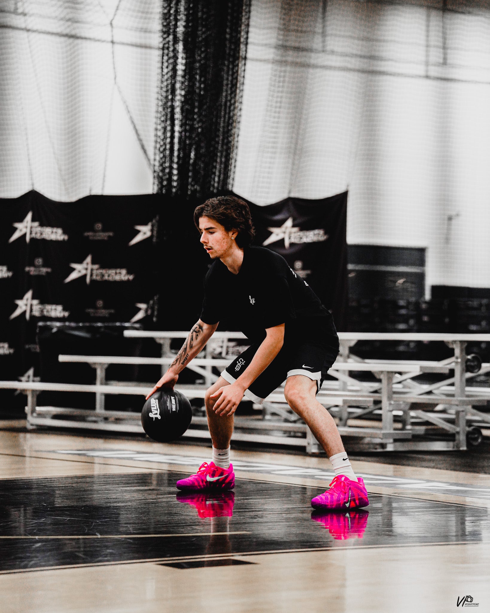 Basketball player in a low stance dribbling a black LVLUP Handle heavy ball on an indoor court, wearing all-black training gear and bright pink basketball shoes.
