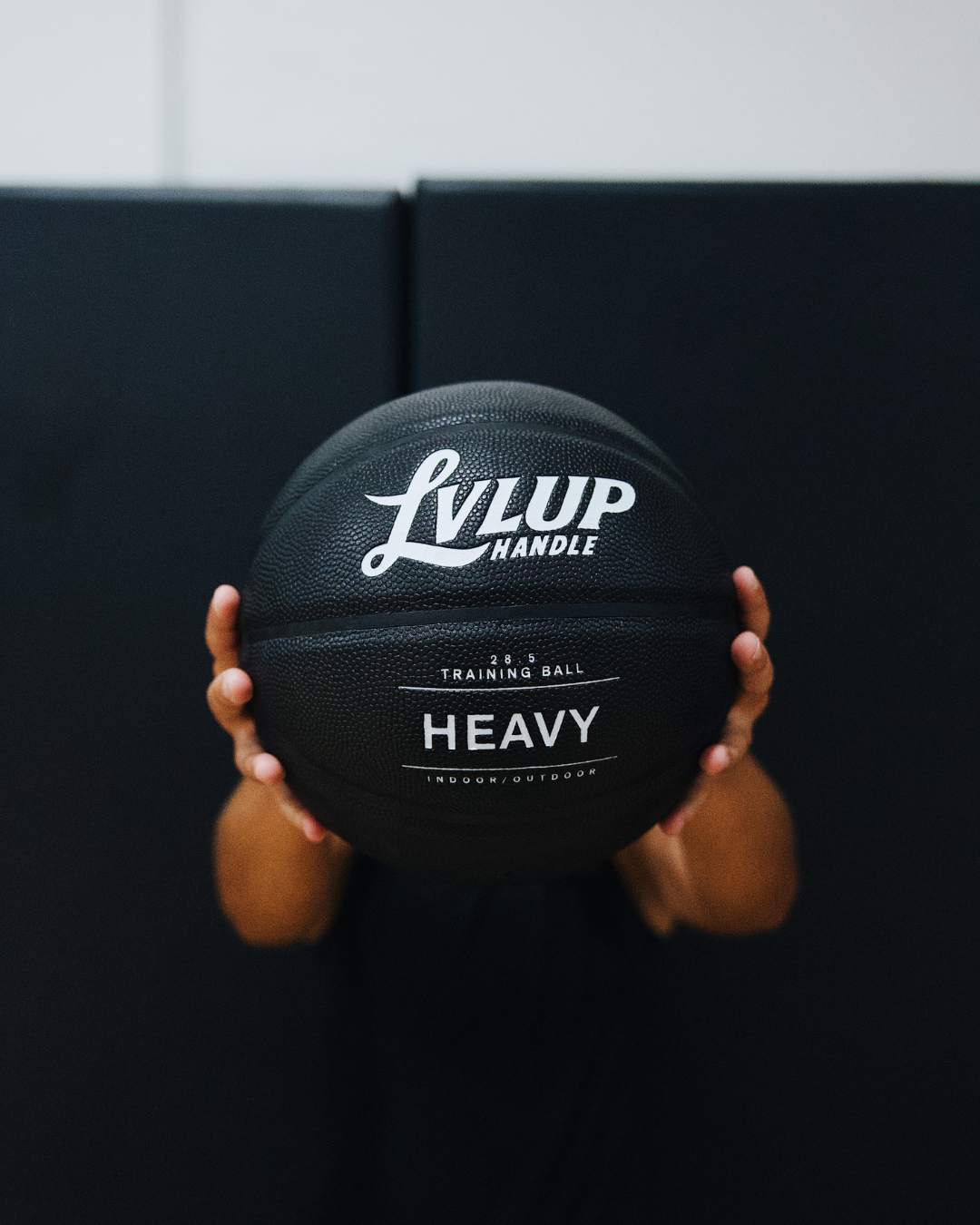 Person holding a black basketball with 'LVLUP' branding against a dark background