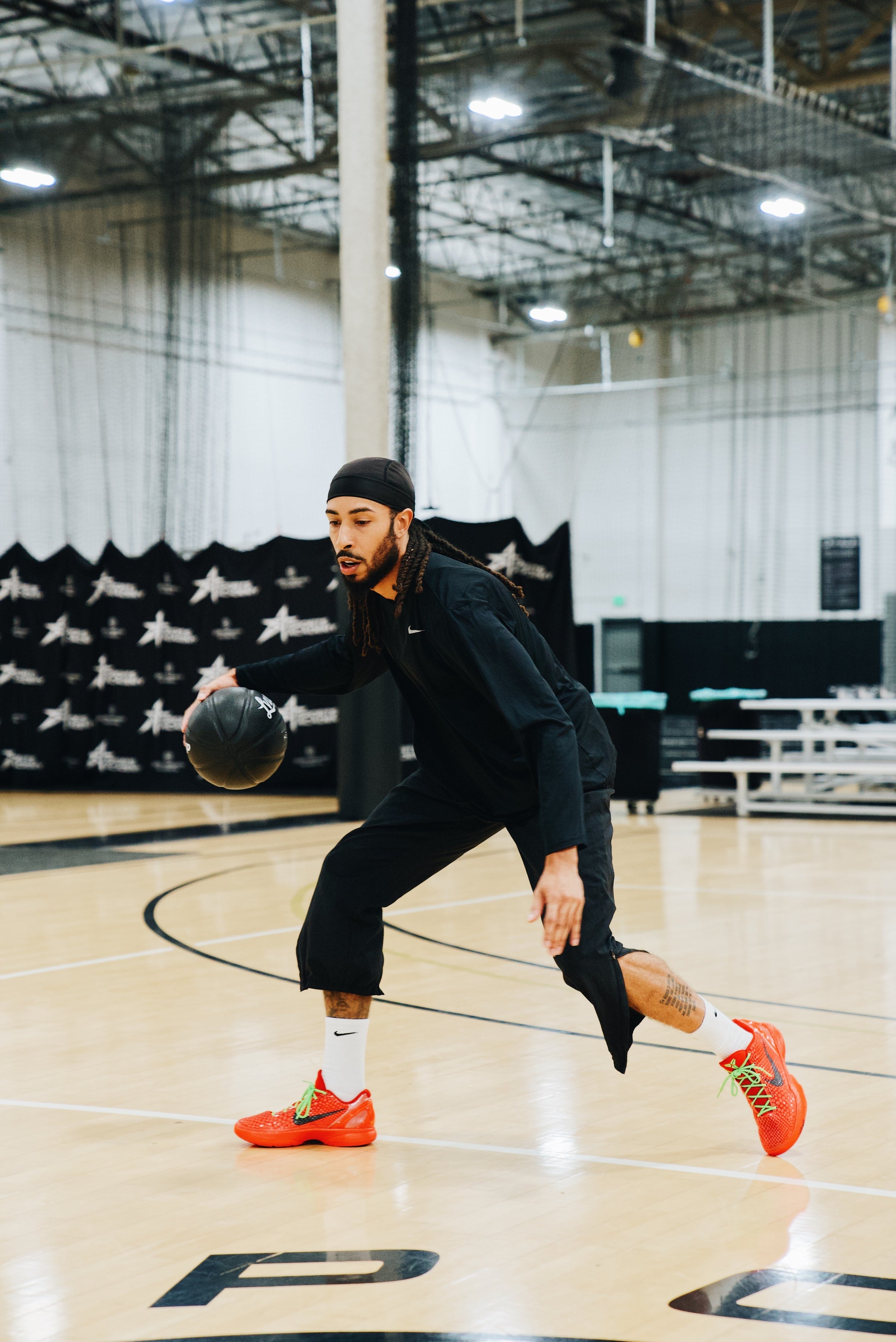 Basketball player in all-black athletic gear dribbling a black LVLUP Handle heavy ball on an indoor court, wearing bright red sneakers and maintaining a low, controlled stance.
