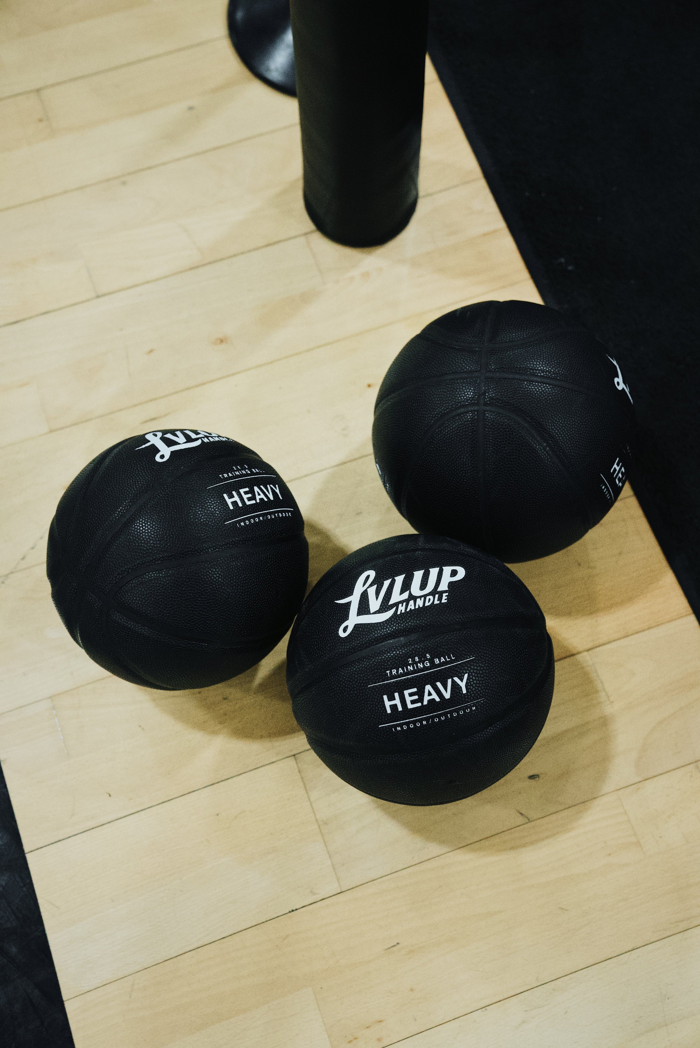 Three black LVLUP Handle Heavy training basketballs resting on a hardwood court, showing the logo and textured surface.